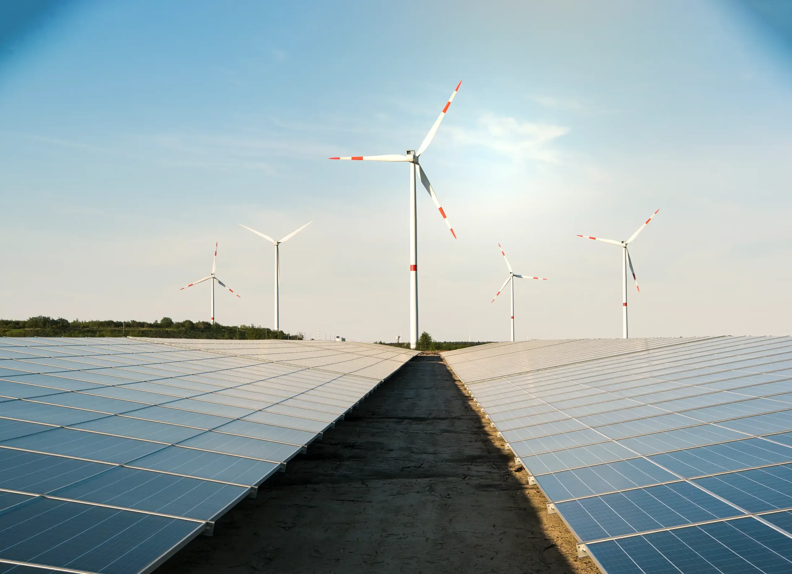 Offene Landschaft mit Solaranlagen im Vordergrund und Windrädern im Hintergrund